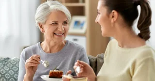 Two women sitting otgether and eating cake.