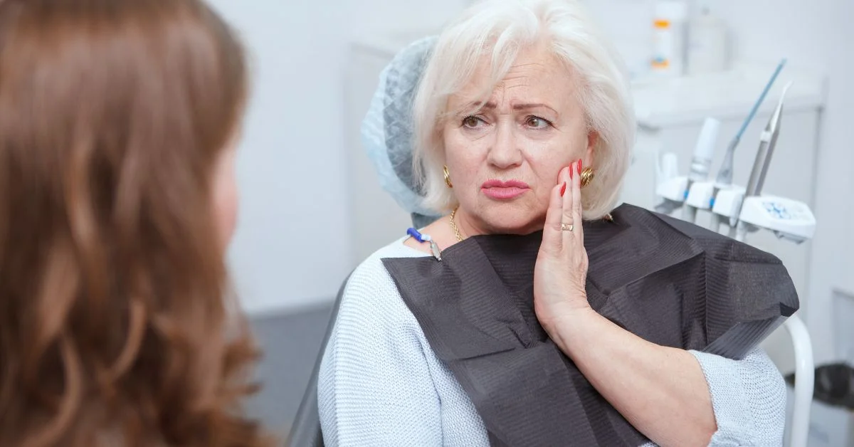 A denture patient sits in a clinic, speaking to their CDT about denture pain.